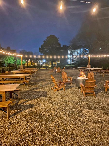 Outdoor Beer Garden at dusk with illuminated hanging lights, picnic tables, Adirondack chairs, and fire pits
